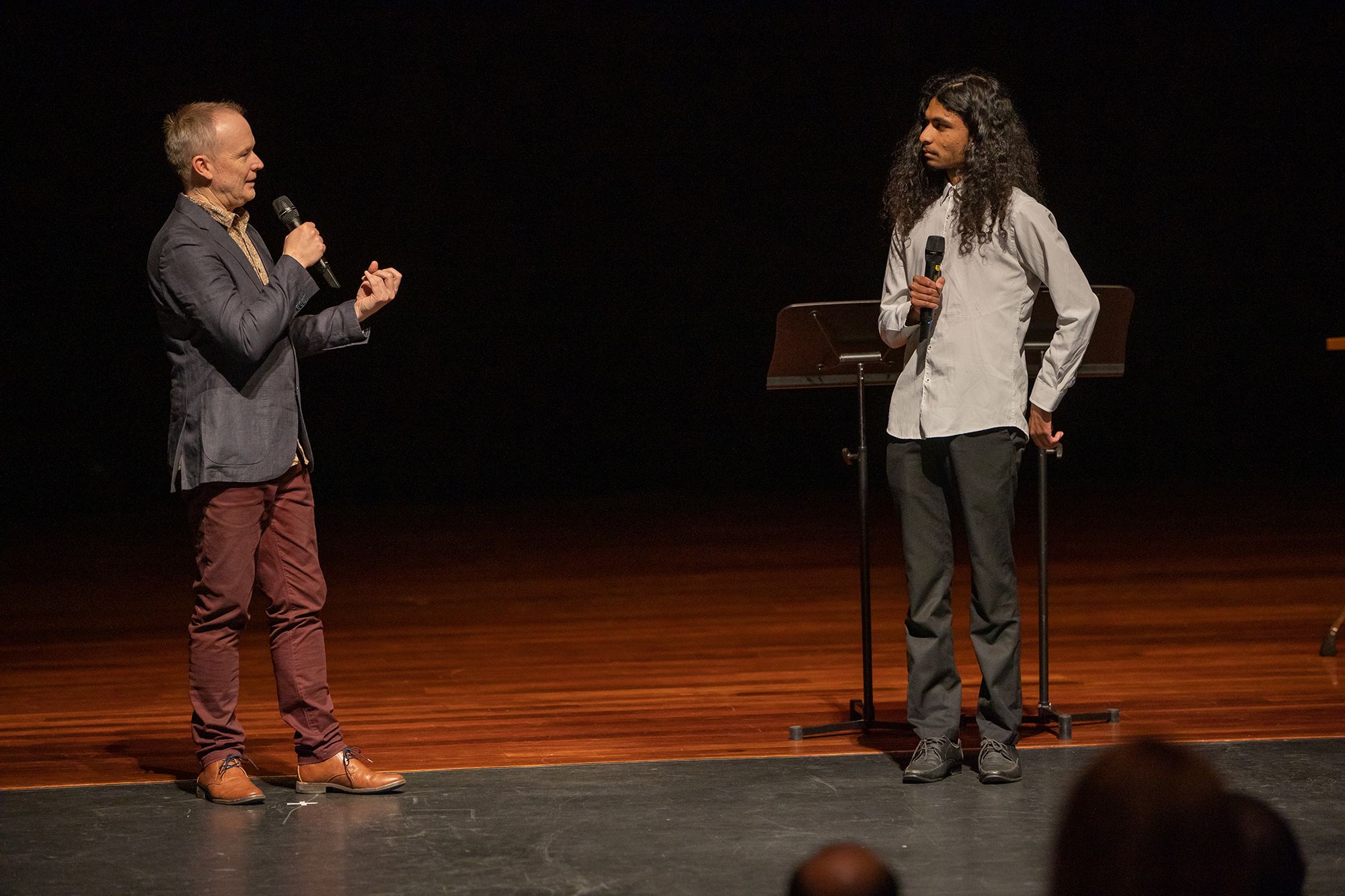 James Ledger and Victor Arul stand on stage for live discussion, speaking into microphones before an audience.