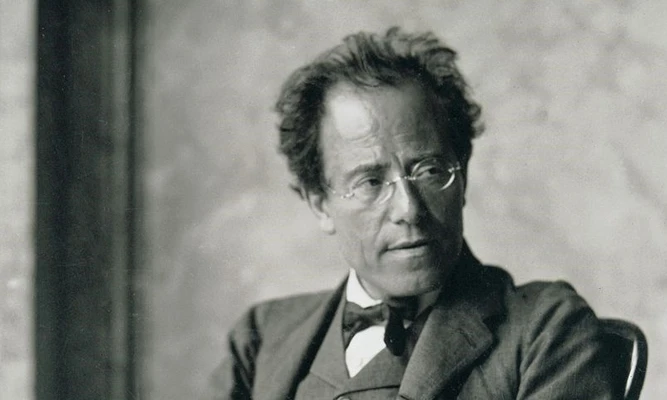 Gustav Mahler sitting in a chair, wearing a three-piece suit and bow tie, with hands folded in his lap