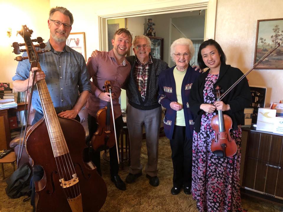 Three WASO string musicians holding their instruments alongside patrons Peter and Jean Stokes.