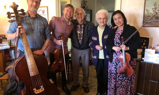 Three WASO string musicians holding their instruments alongside patrons Peter and Jean Stokes.