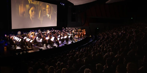 WASO performs on stage at the River Side Theatre, PCEC, with a large screen behind the orchestra displaying a James Bond film