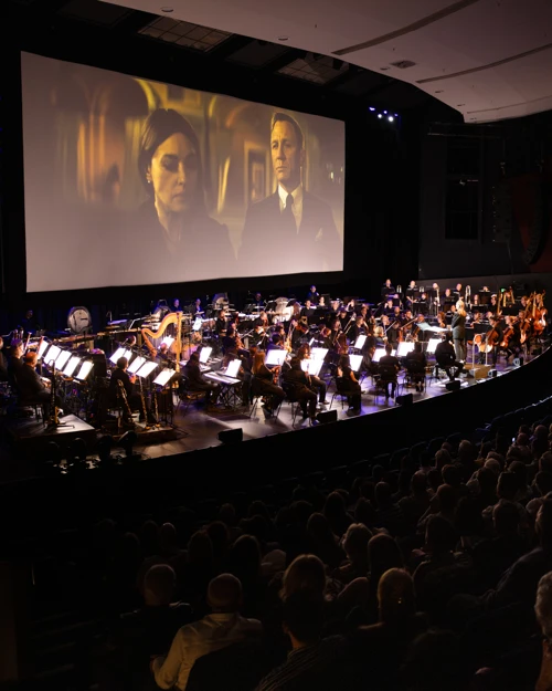 Movie Time! WASO performs on stage at the River Side Theatre, PCEC, with a large screen behind the orchestra displaying a James Bond film