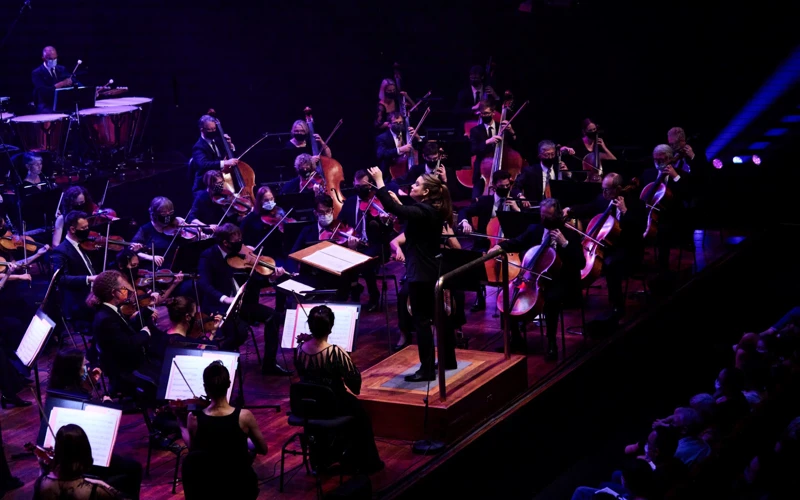 Jen Winley conducting an orchestra under dim purple stage lights.