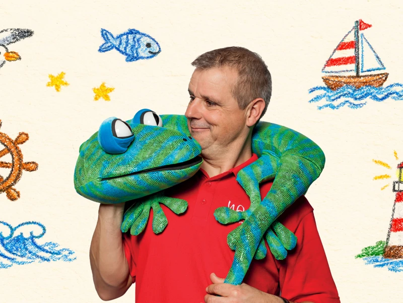 Browse Events An event banner for Echo the Gecko in which a man holds a lizard puppet and is surrounded by drawings of the seaside
