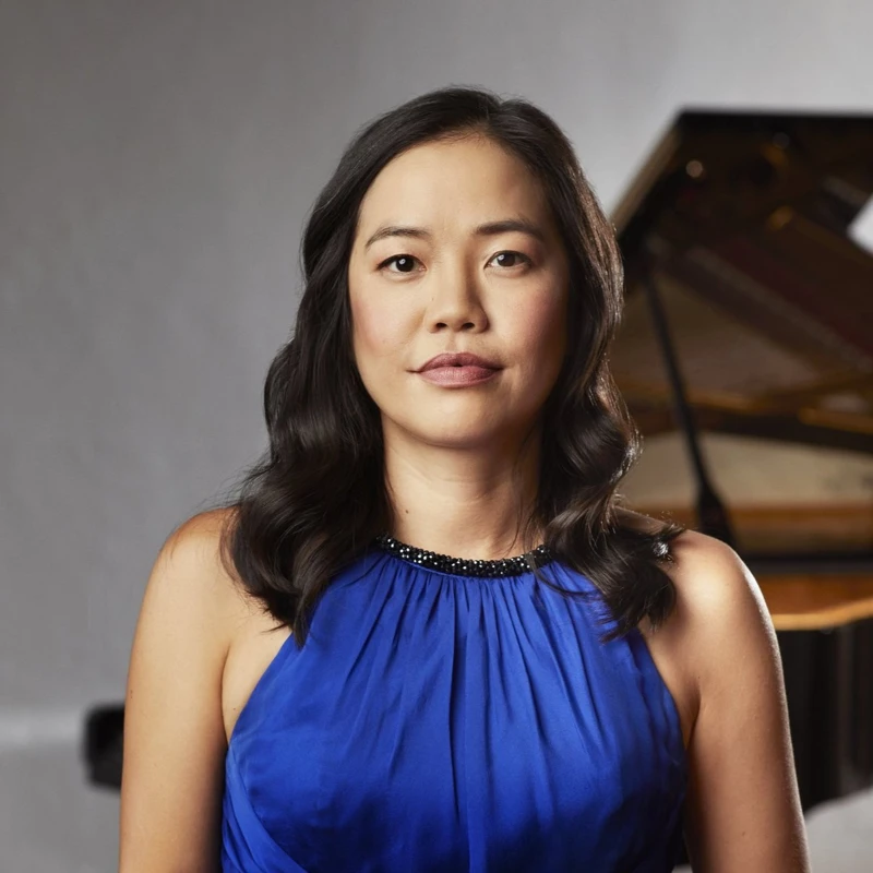 Headshot of Andrea Lam wearing a blue satin dress in front of a grand piano.