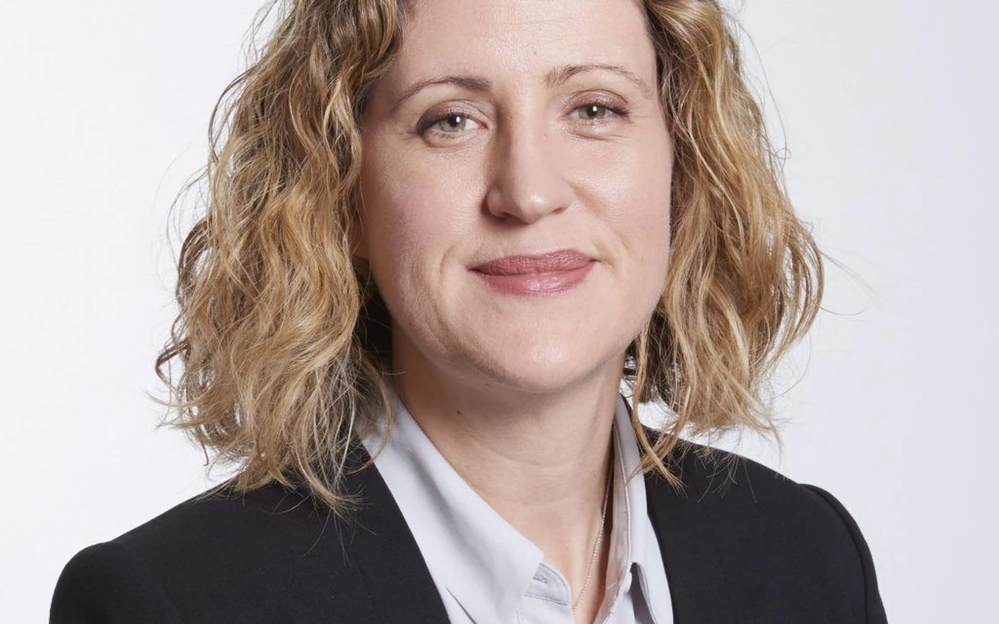 Professional headshot of Alex Willcocks wearing a white collared shirt and black blazer.