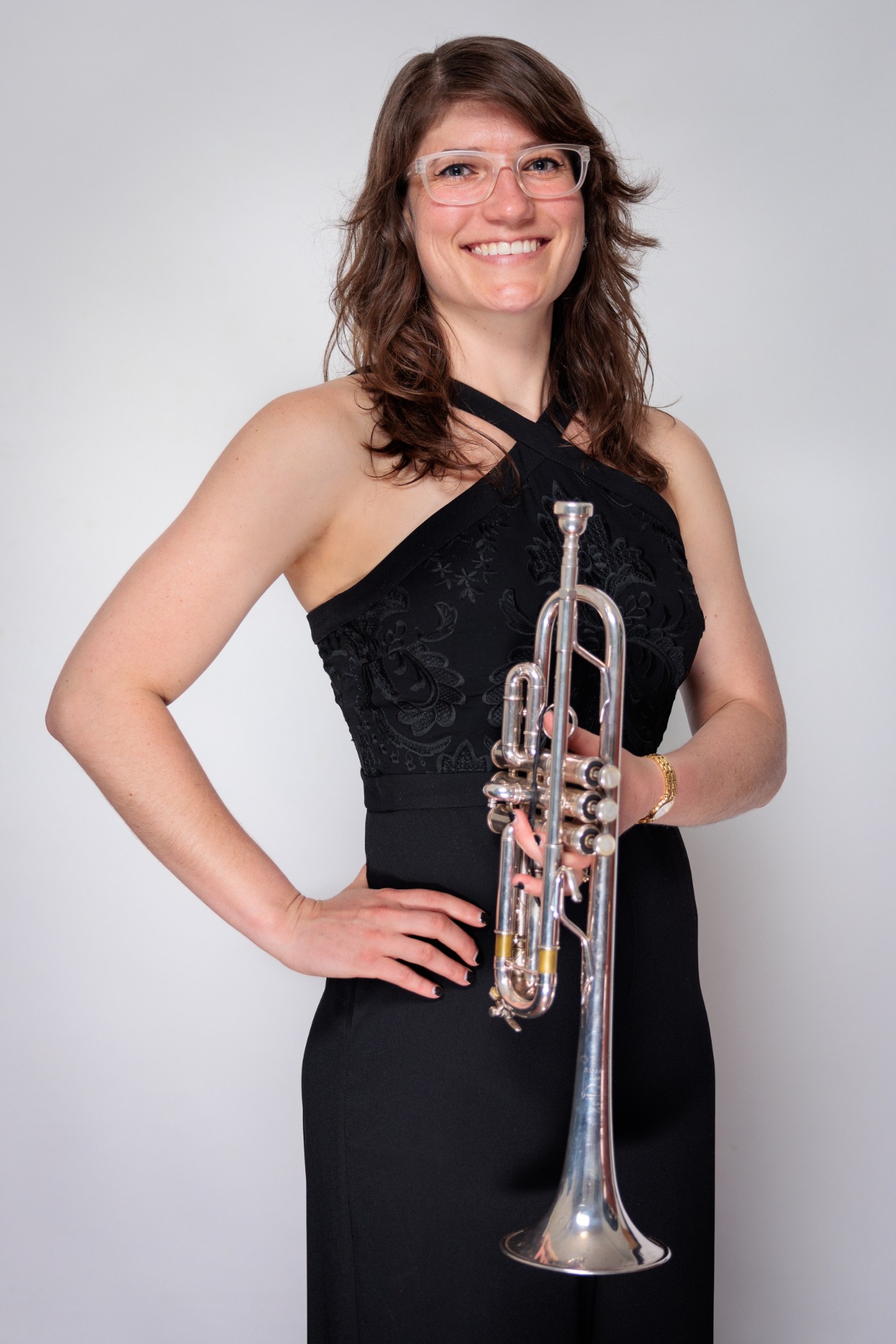 Headshot of Jenna Smith wearing a black halter-neck gown and glasses, holding a trumpet.