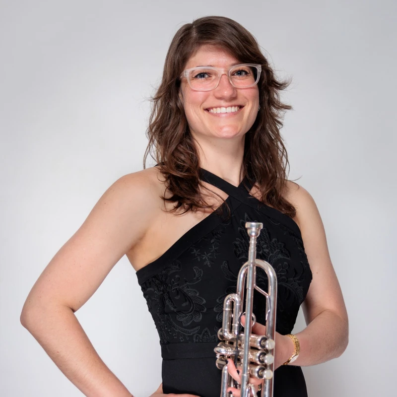 Headshot of Jenna Smith wearing a black halter-neck gown and glasses, holding a trumpet.