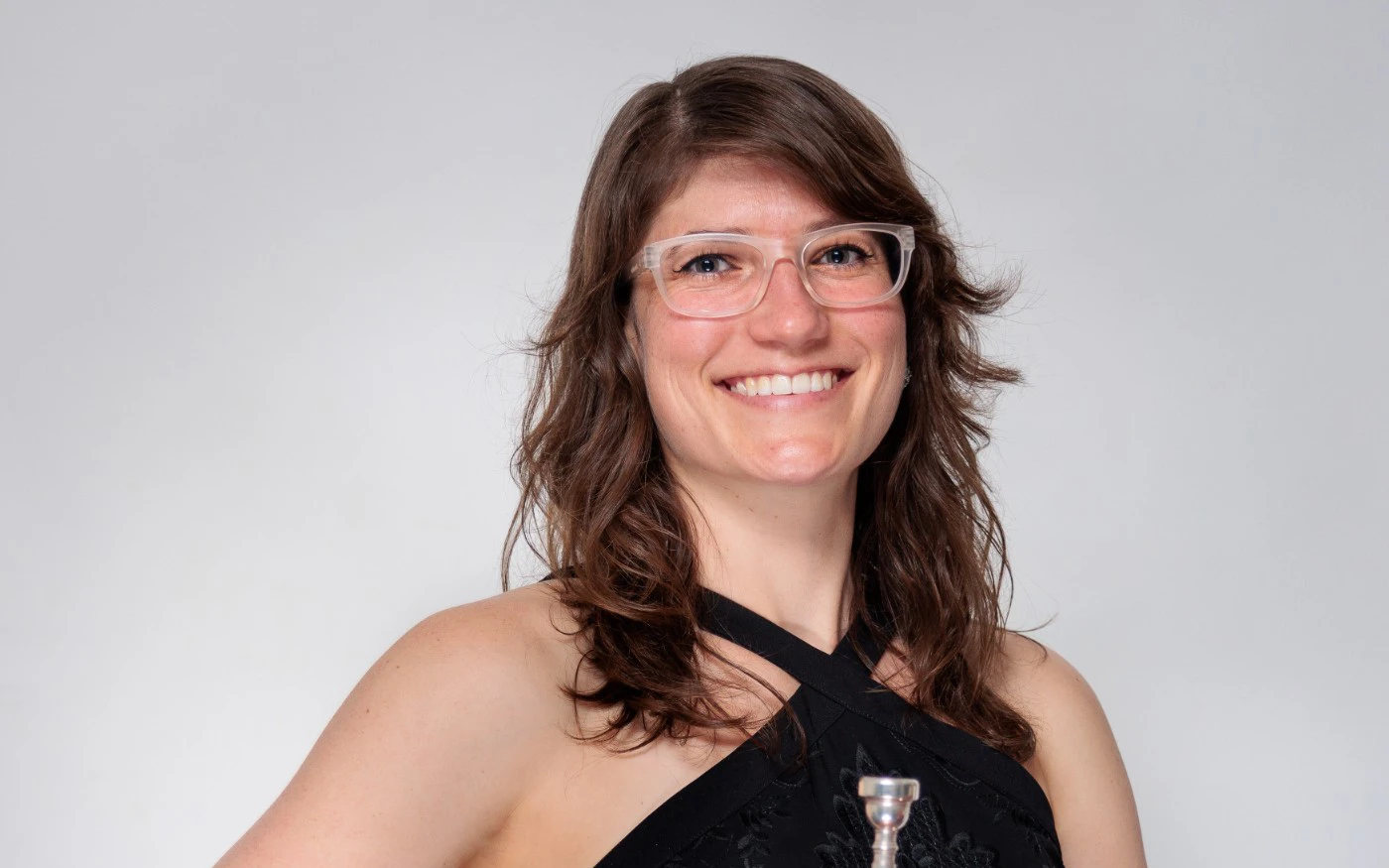 Headshot of Jenna Smith wearing a black halter-neck gown and glasses, holding a trumpet.