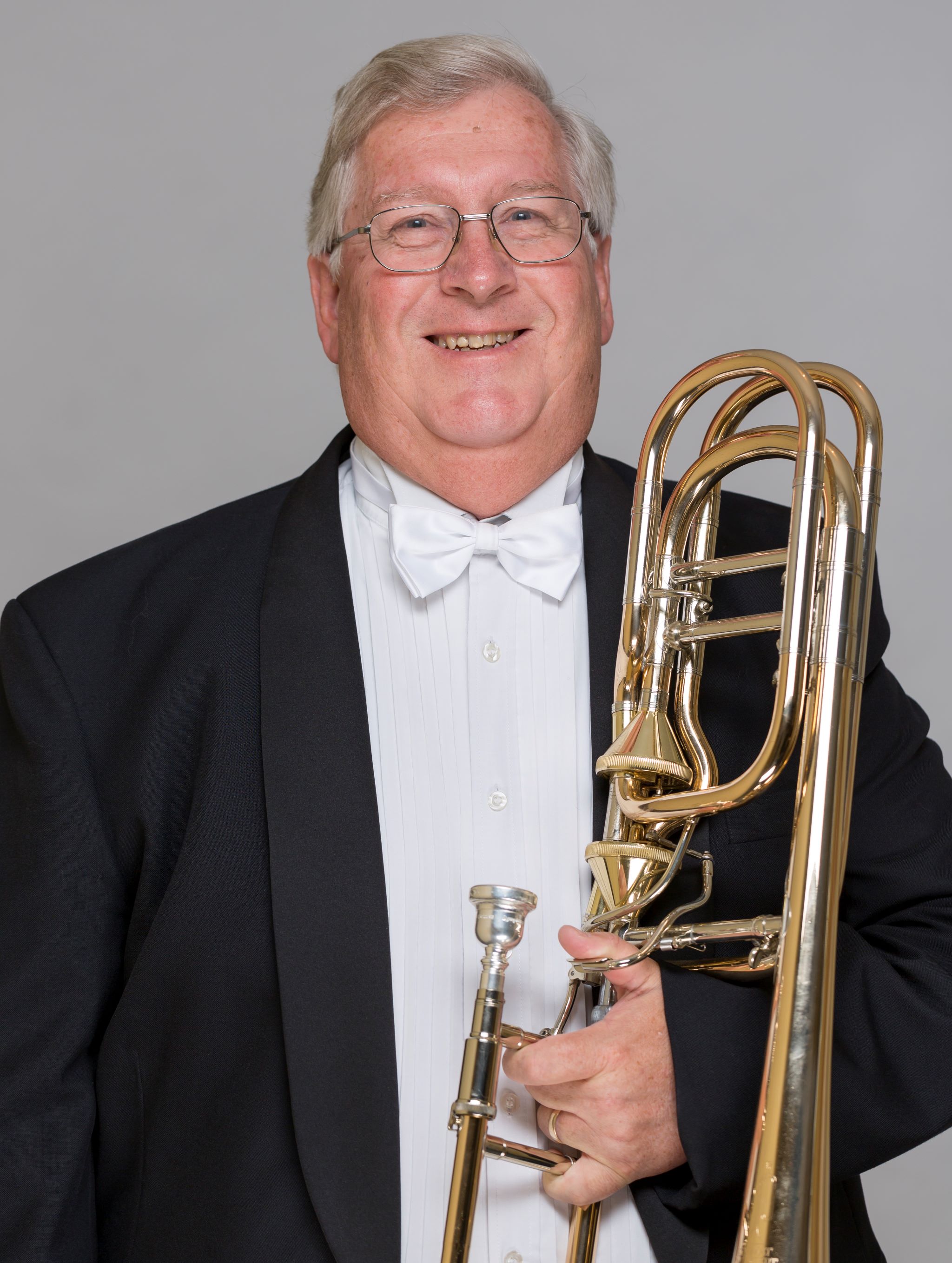 Headshot of Philip Holdsworth dressed in a formal suit, holding a trombone.