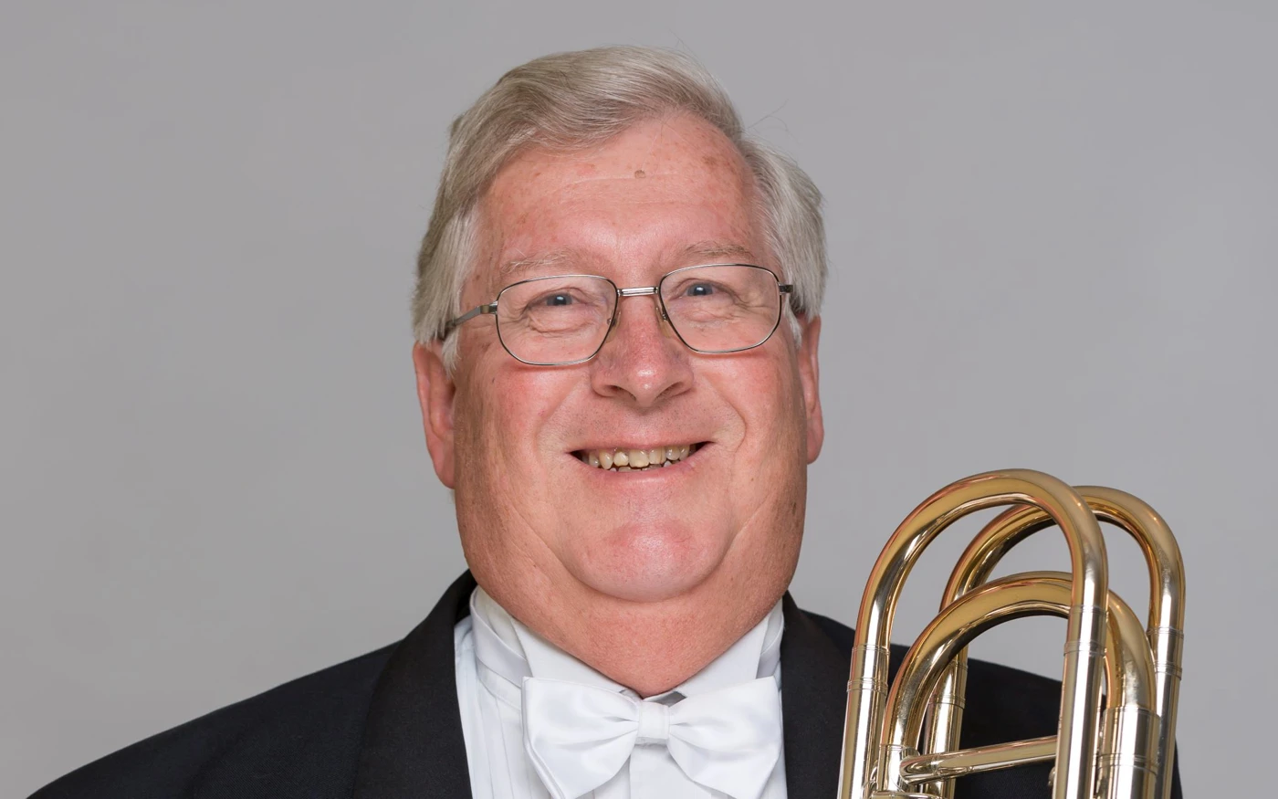 Headshot of Philip Holdsworth dressed in a formal suit, holding a trombone.