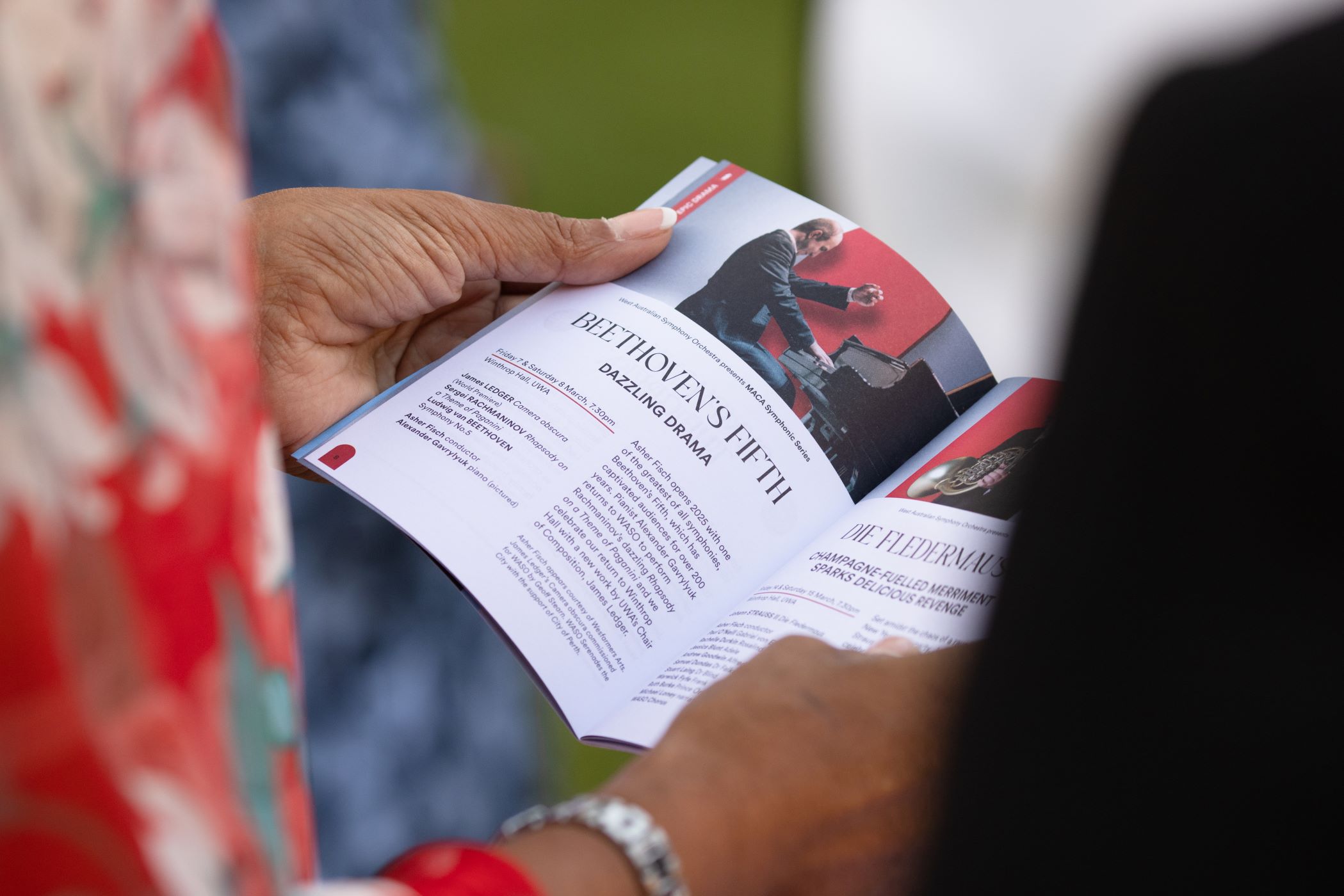 Looking over the shoulder of a concert attendee who is holding a printed concert program.