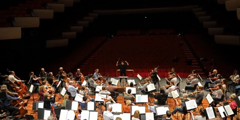 A conductor is in motion conducting an orchestra rehearsal at Perth Concert Hall