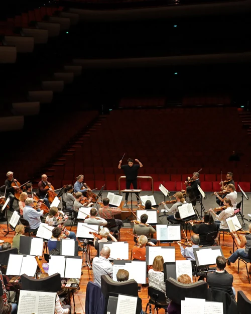 Learn More A conductor is in motion conducting an orchestra rehearsal at Perth Concert Hall
