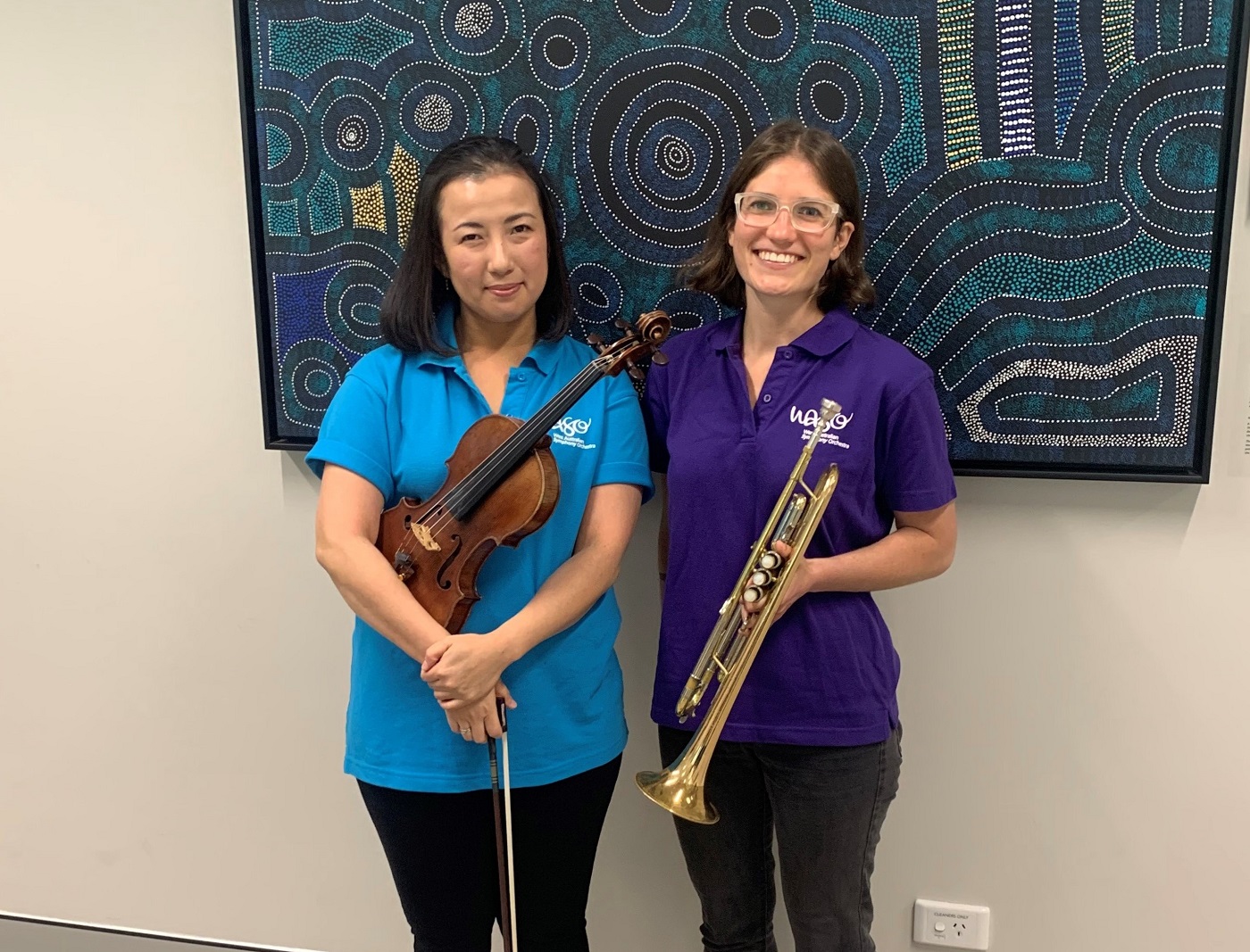 A violinist and trumpet player pose side-by-side, wearing colourful WASO polo shirts.
