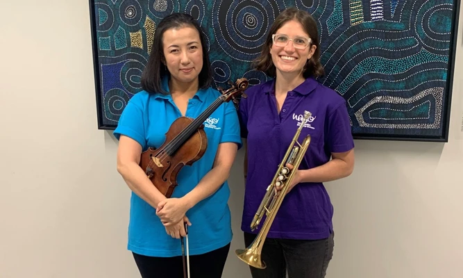 A violinist and trumpet player pose side-by-side, wearing colourful WASO polo shirts.