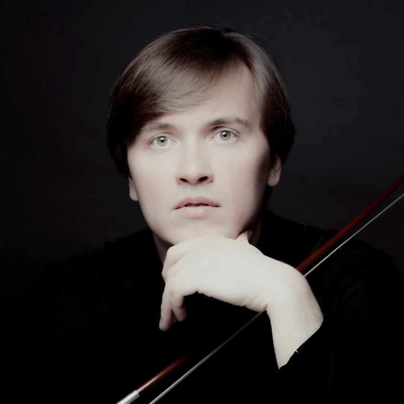 Headshot of Ivan Karizna in dark studio lighting, holding a cello bow.