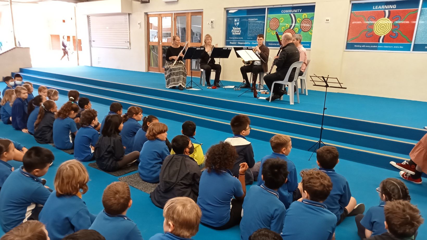 A WASO wind quintet performs for a group of primary school students seated on the floor.