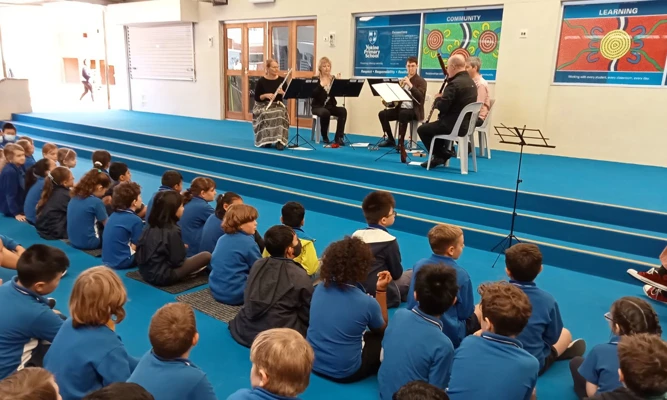 A WASO wind quintet performs for a group of primary school students seated on the floor.