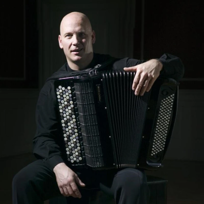 Headshot of James Crabb wearing a black shirt and pants, sitting with an accordion on his knee.