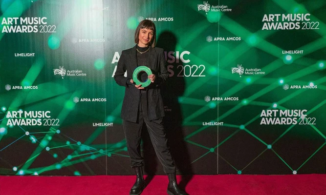 Olivia Davies poses with a trophy on the red carpet of the Art Music Awards 2022, wearing a black pantsuit and boots.