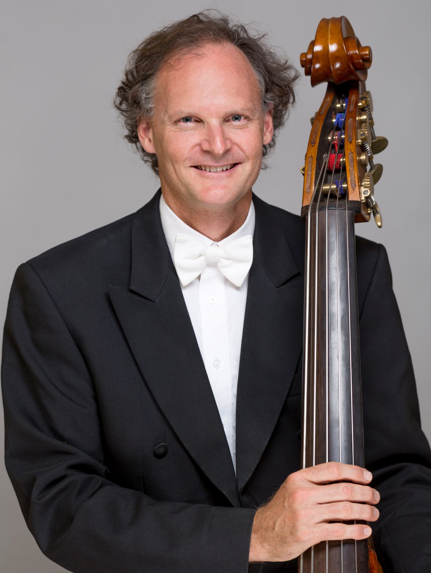 Headshot of Andrew Sinclair wearing a formal suit, holding a double bass.