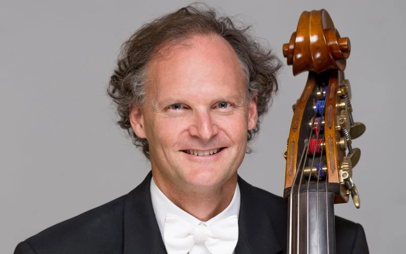 Headshot of Andrew Sinclair wearing a formal suit, holding a double bass.