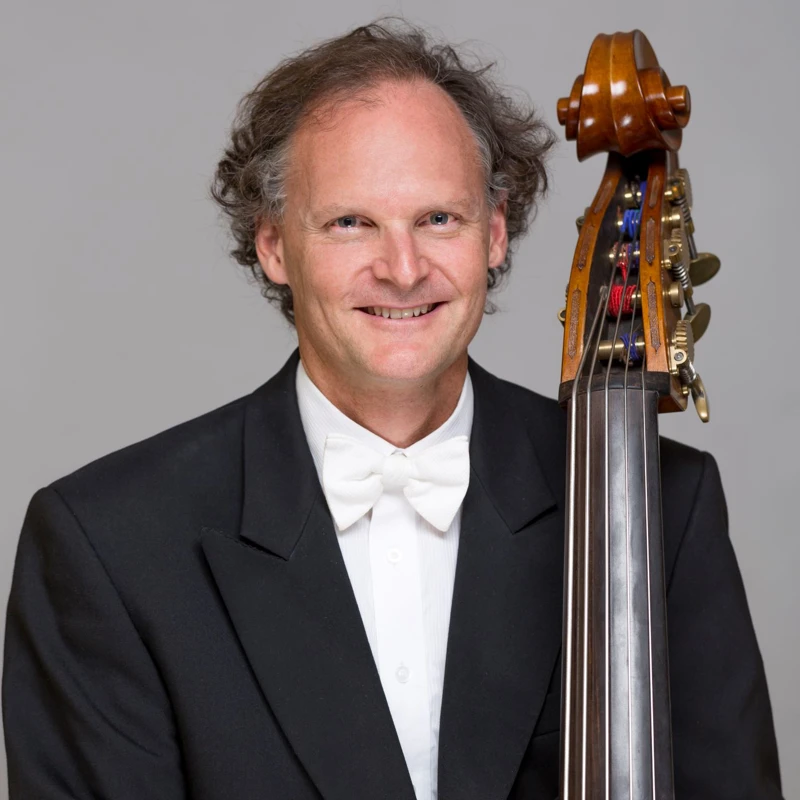 Headshot of Andrew Sinclair wearing a formal suit, holding a double bass.