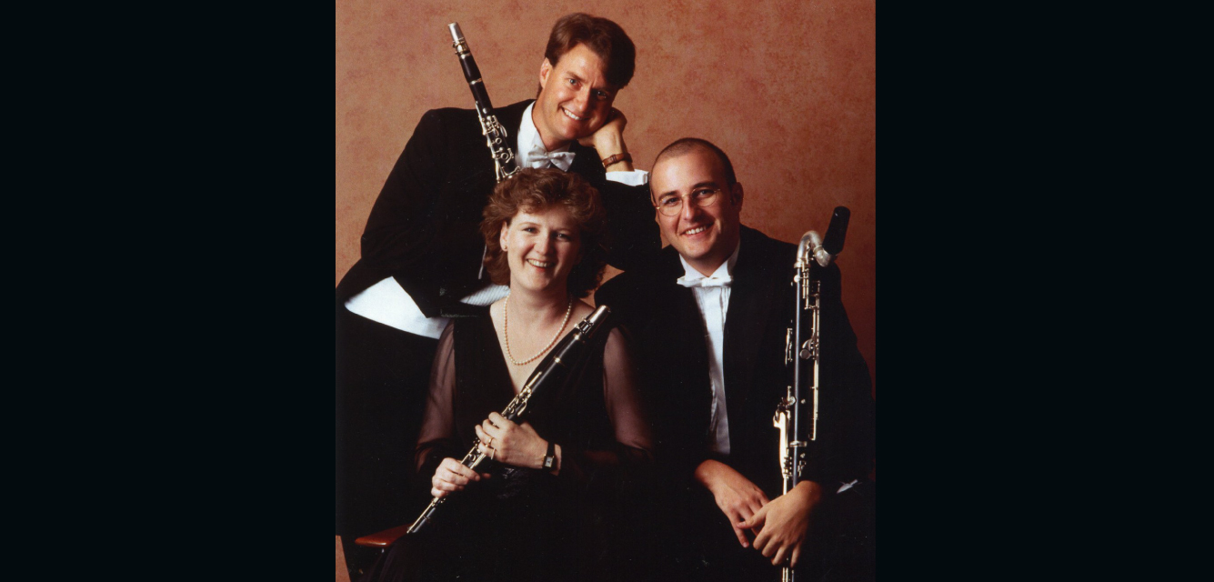 Three woodwind musicians pose with clarinet-family instruments in a formal studio portrait.