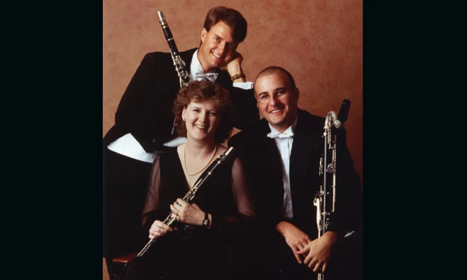 Three woodwind musicians pose with clarinet-family instruments in a formal studio portrait.
