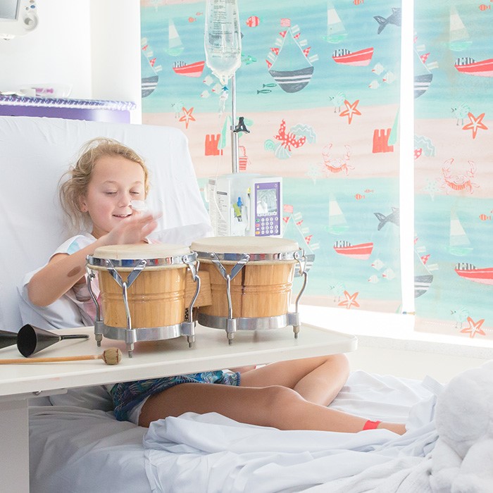 A young girl in a hospital bed plays a set of bongo drums
