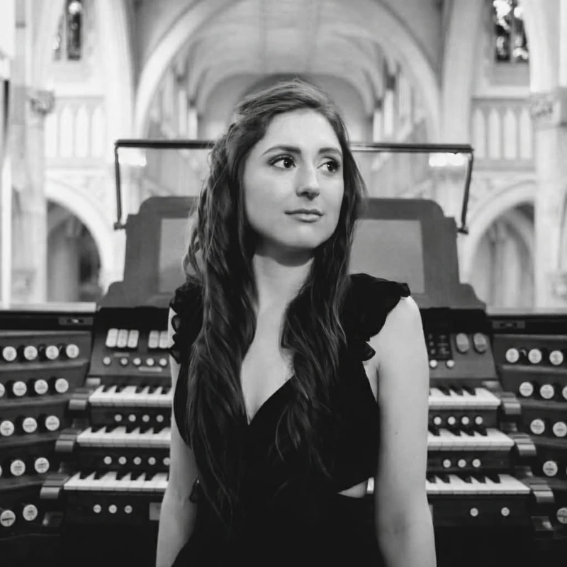 Black & white headshot of Holly Broadbent wearing a black dress in front of a pipe organ.