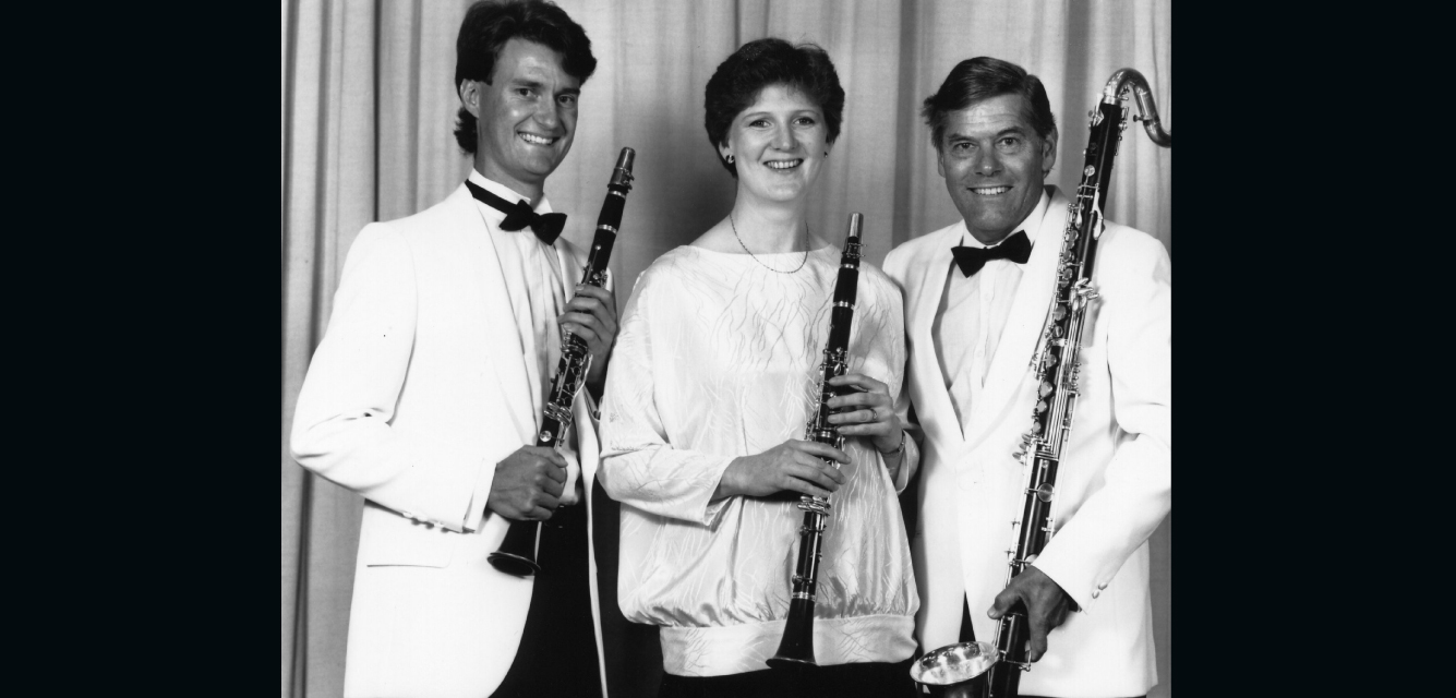Three woodwind musicians pose with clarinets and bass clarinet in a formal, black & white group portrait.