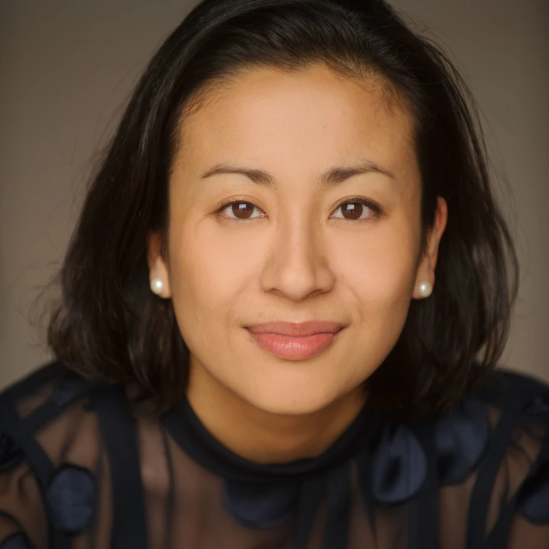 Headshot of Aura Go wearing a dark sheer top and white pearl earrings.