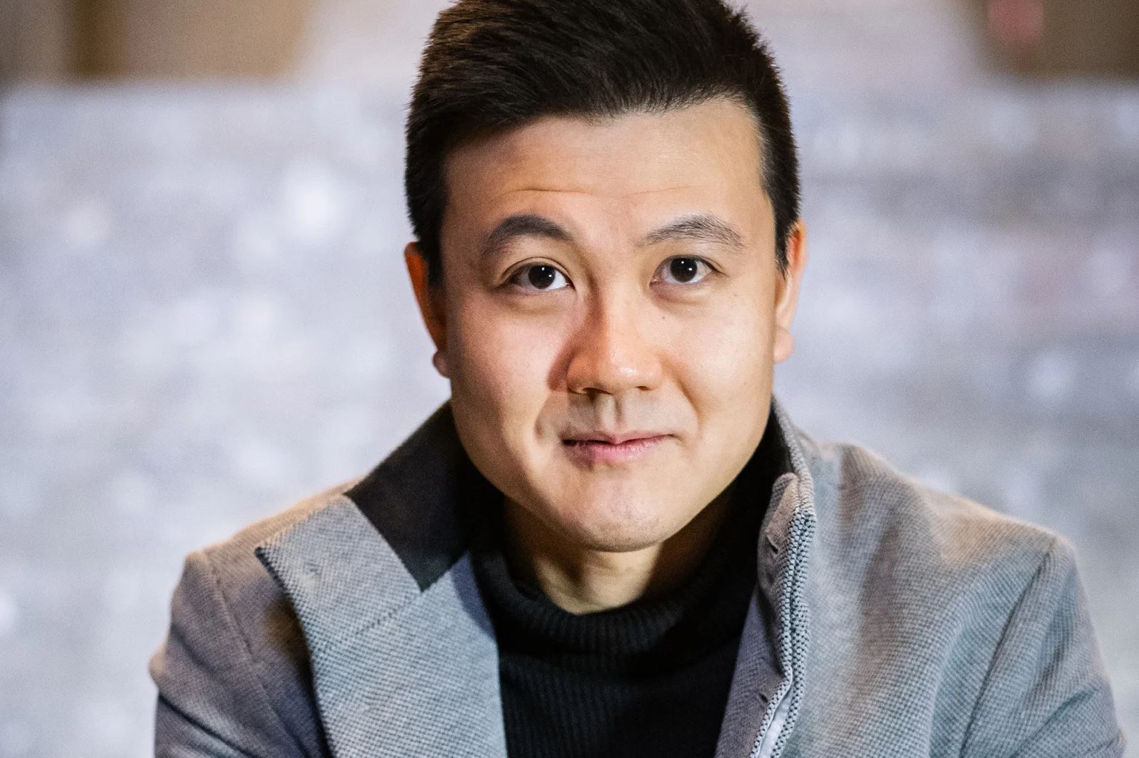 Headshot of Thaddeus Huang wearing a grey jacket and black shirt.