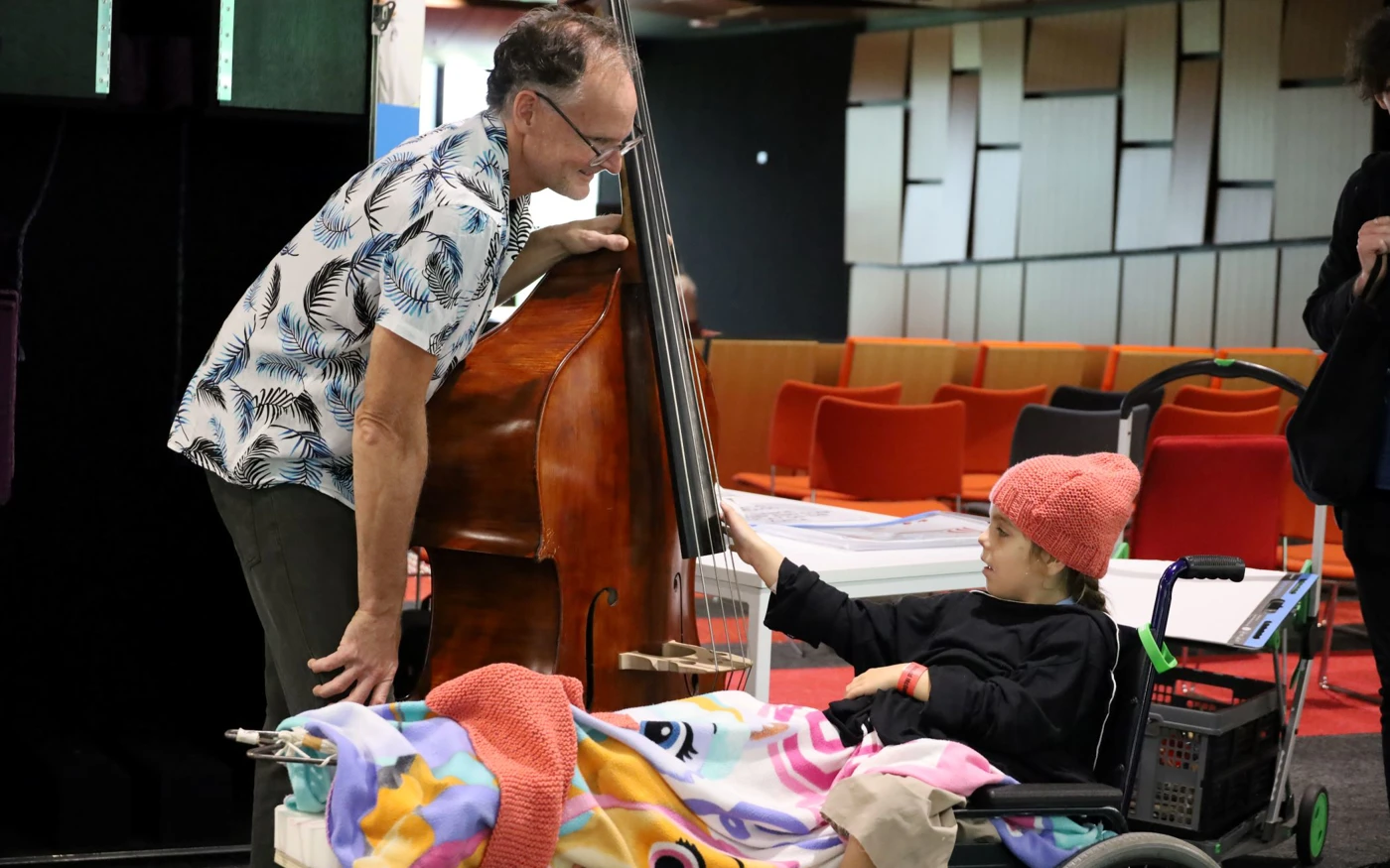 A double bass player showing his instrument to a young hospital patient in a wheelchair.