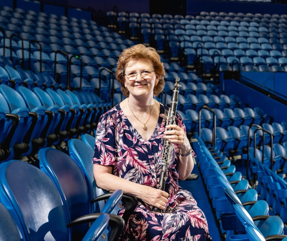 Lorna Cook sitting among arena-style seating, holding a clarinet.