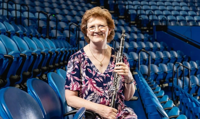 Lorna Cook sitting among arena-style seating, holding a clarinet.