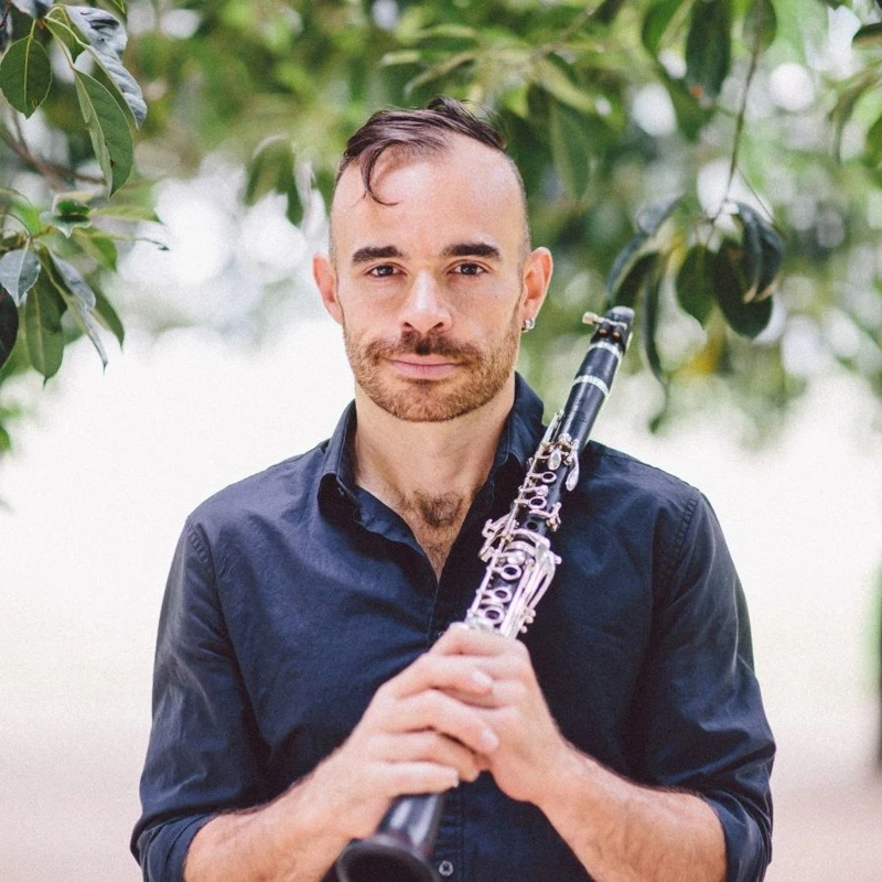 Headshot of Ashley Smith wearing a navy collared shirt, resting a clarinet on his shoulder.