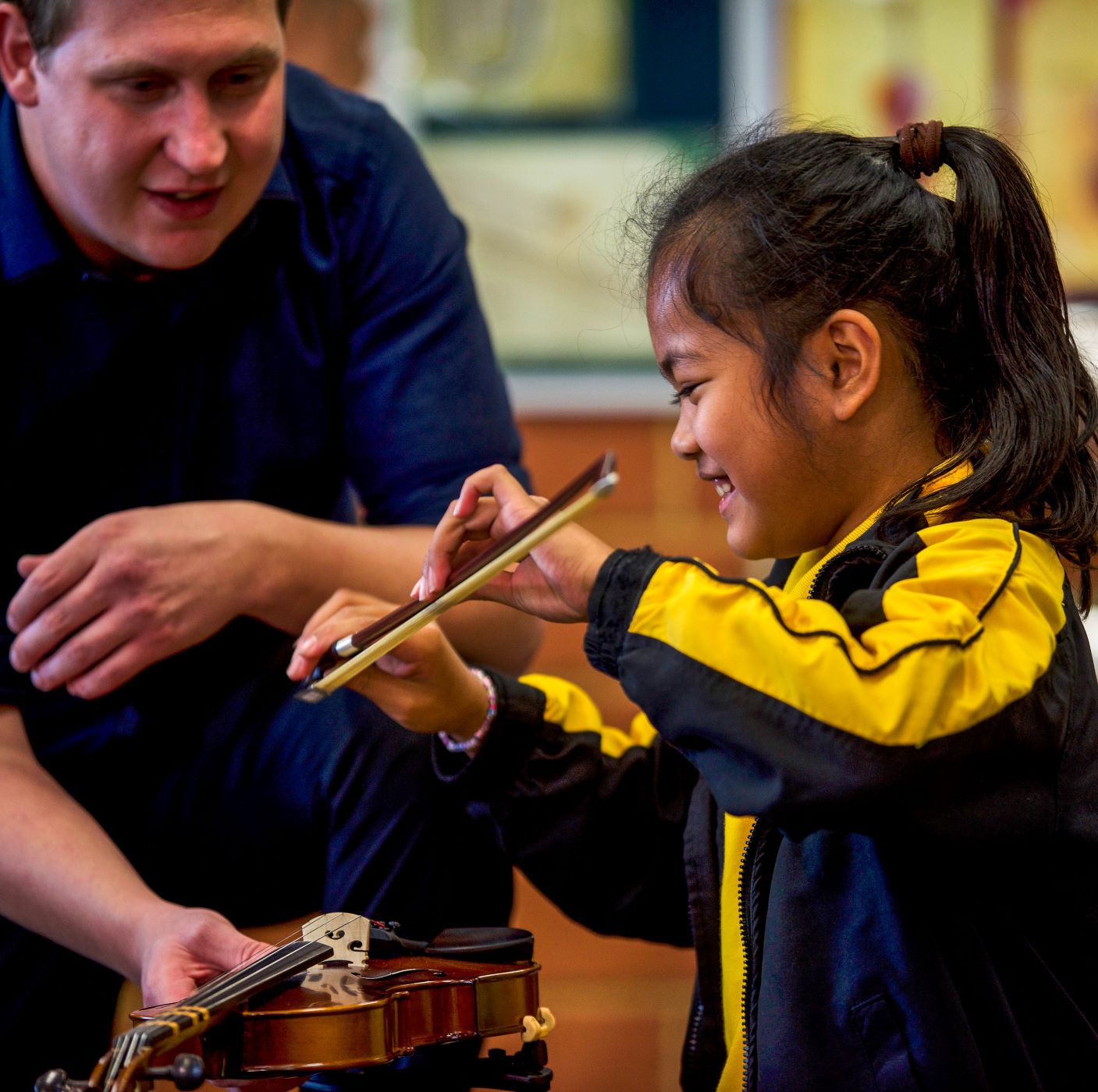 Close up side profile of smiling student learning how to hold a violin bow.