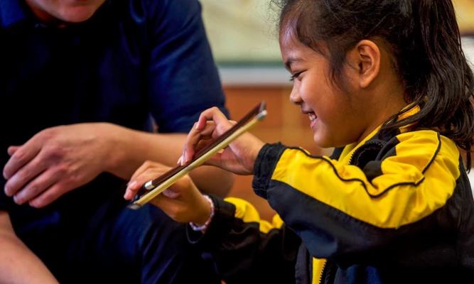 Close up side profile of smiling student learning how to hold a violin bow.