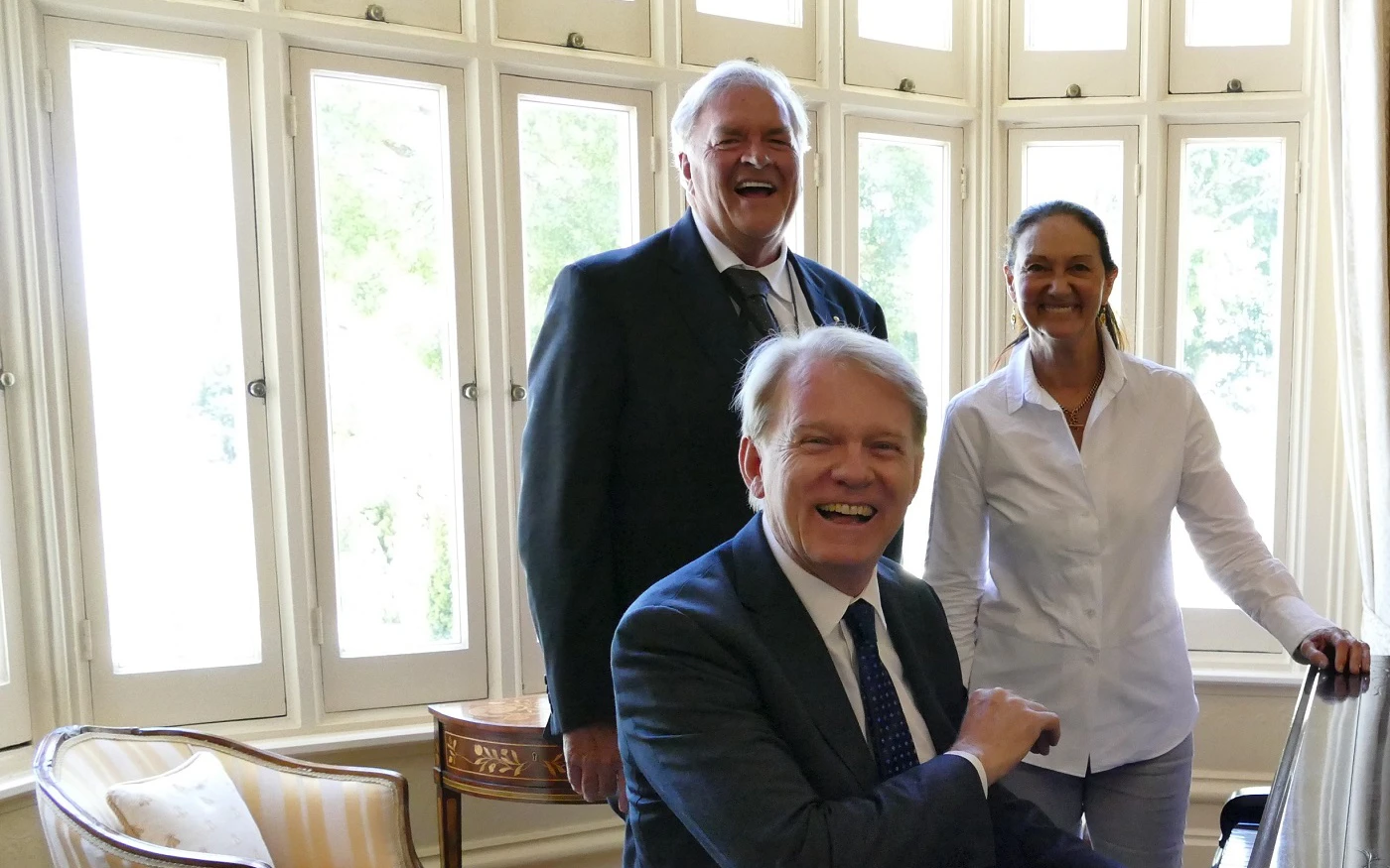 Hon. Kim Beazley AC, Susie Annus Beazley and Mark Coughlan smile for a group photo around a piano.