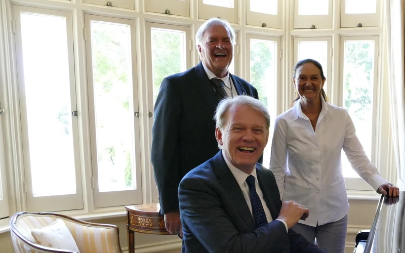 Hon. Kim Beazley AC, Susie Annus Beazley and Mark Coughlan smile for a group photo around a piano.