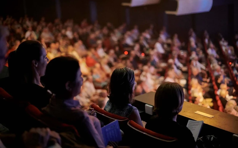 First Timer's Guide Audience members seated in the balcony of Perth Concert Hall watch a live orchestral performance, with the brightly lit stage out of frame and the rest of the auditorium softly blurred in the background.