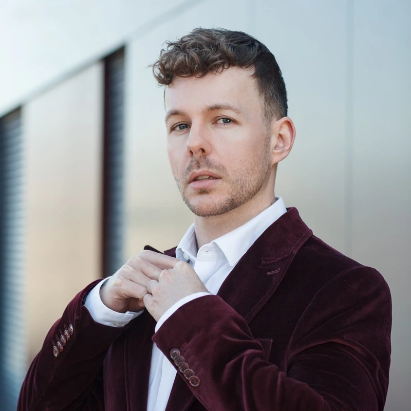 Headshot of Alasdair Kent wearing a maroon suit jacket and white shirt.