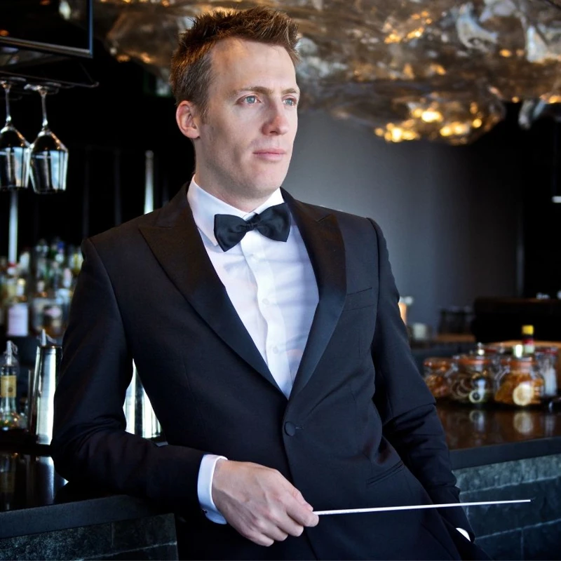 Headshot of Nicholas Buc wearing a black tuxedo and holding a baton.