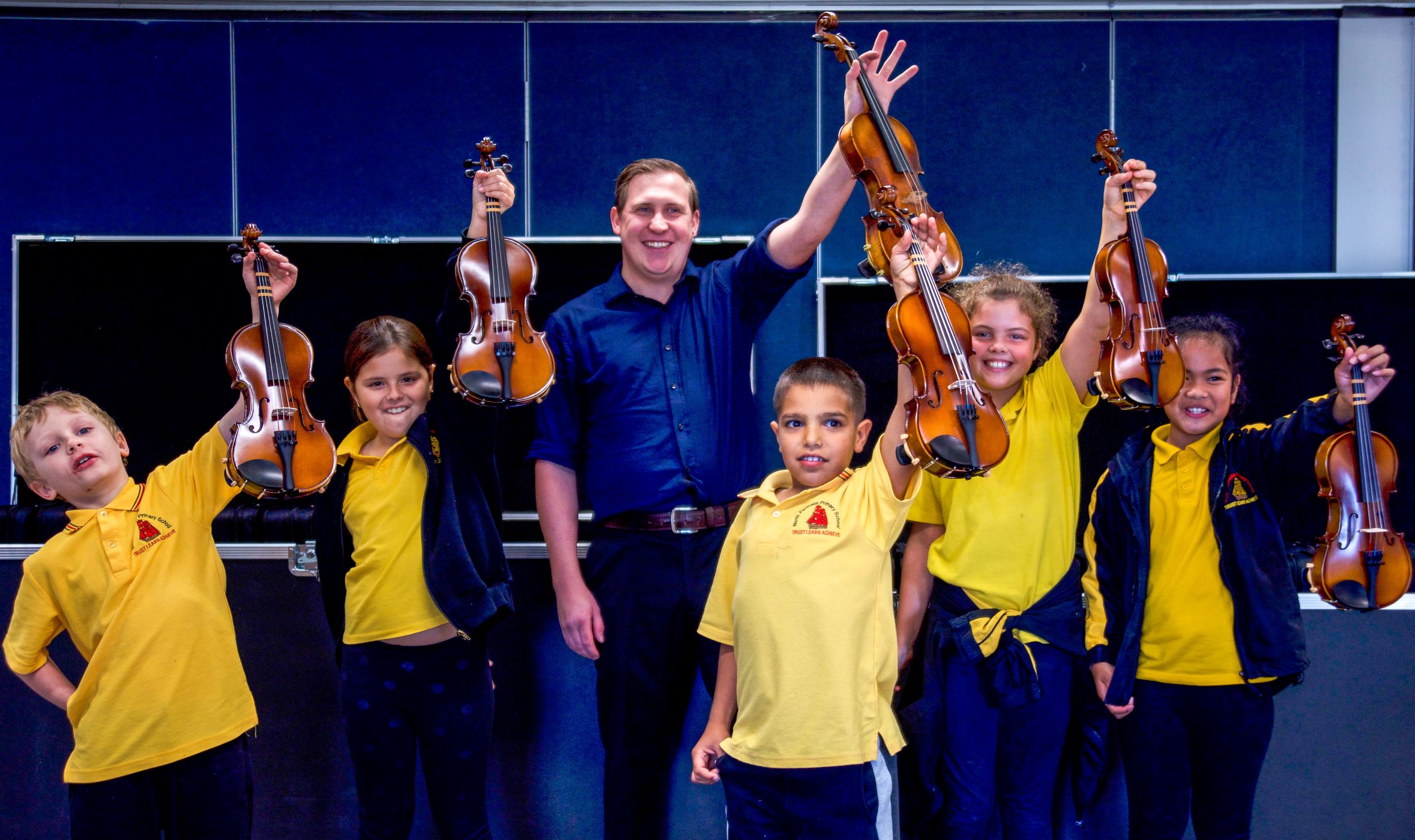 Group of Crescendo students and their teacher smile while holding up their violins.