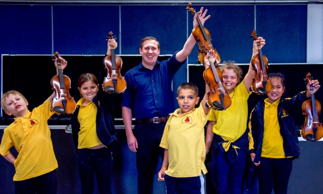 Group of Crescendo students and their teacher smile while holding up their violins.