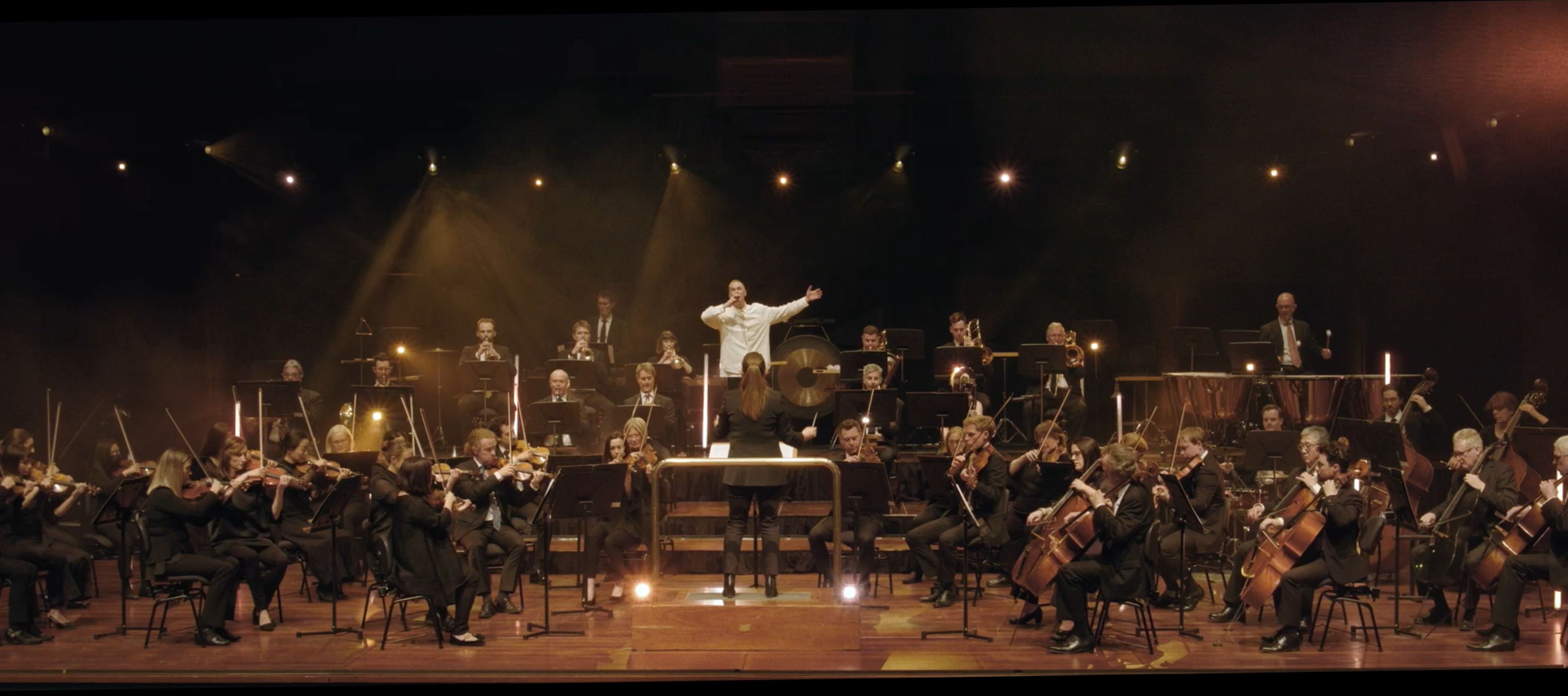 Still from 'Jimmy Recard' music video: Drapht performs on stage with WASO, under dramatic lighting in a dark concert hall.