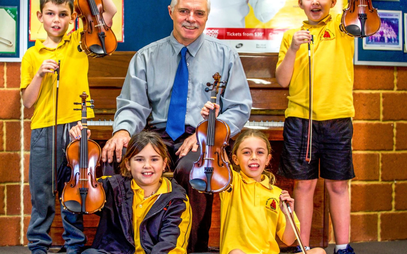 Group of Crescendo students smile while holding up their violins.